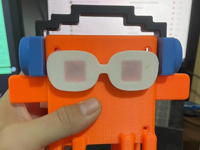 Orange 3D-printed desk companion with a small screen face