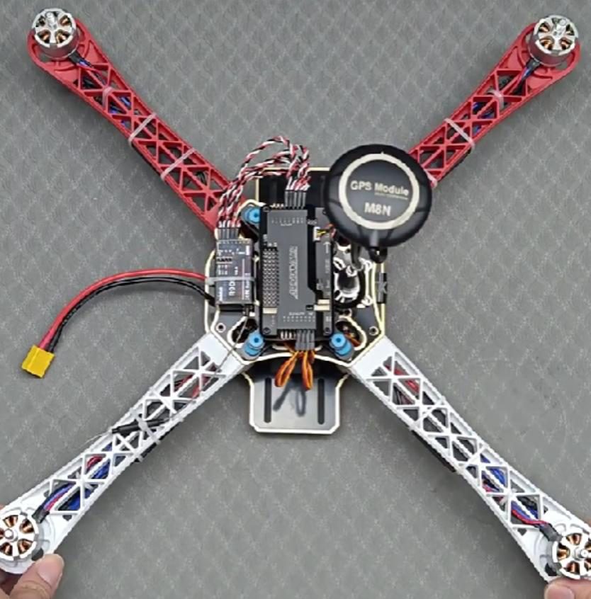 Top view of the quadcopter frame held by two hands, showing the flight controller, GPS module and wiring