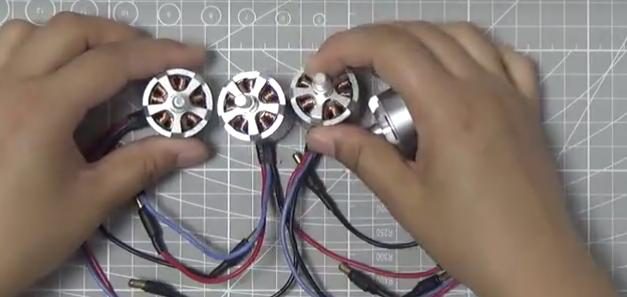 Hands holding four brushless motors with their leads on a cutting mat