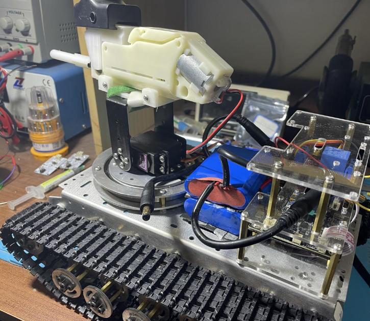 Closer angled view of the tracked robot showing the servo turret, wiring and acrylic electronics enclosure, with lab equipment behind
