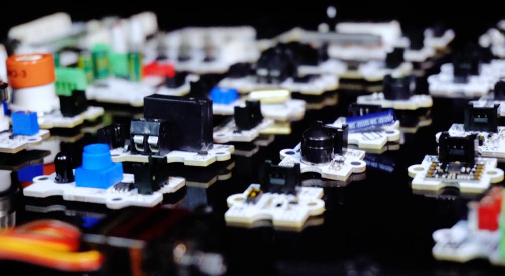 Close-up of many small white sensor modules with blue, black and green components on a glossy black surface