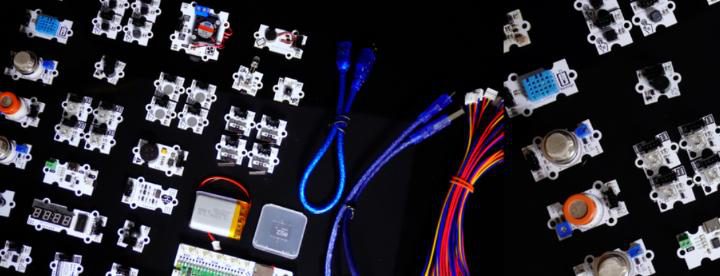Sensor modules, USB cables, a small battery and coloured jumper wires arranged on a black surface