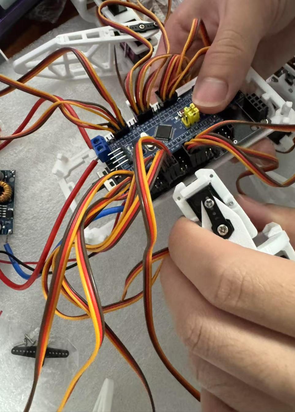 Hands plugging servo cables into a blue STM32 board mounted in a white 3D-printed hexapod frame