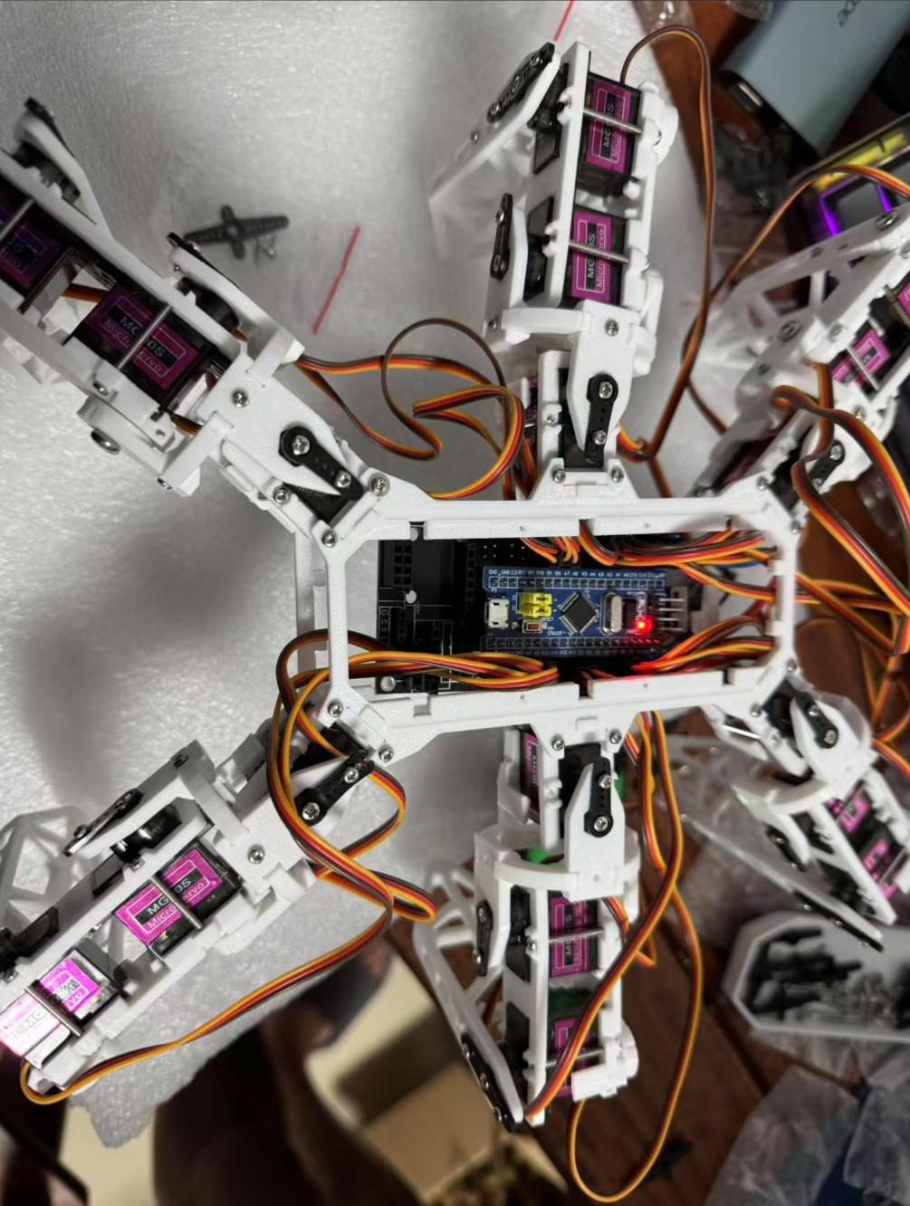 Top view of a white 3D-printed hexapod with purple servos in every leg and the controller board in the center