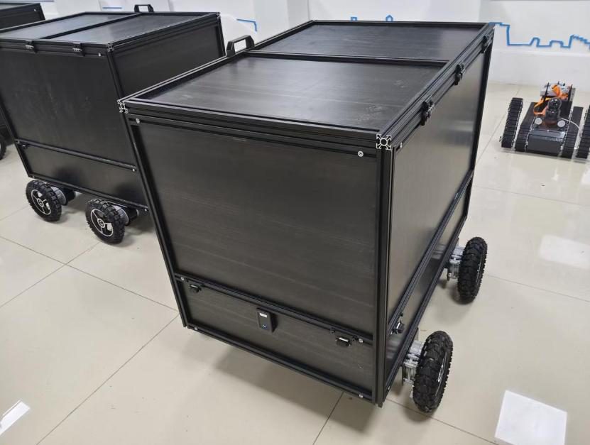 Two black box-shaped delivery robots with chunky air-filled wheels on a tiled floor, a small tracked robot in the background