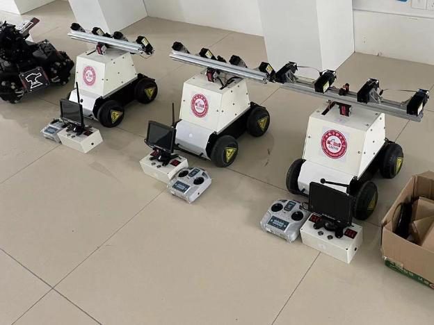 Three white laser weeding robots lined up on a tiled floor, each with an aluminium laser beam on top and a remote controller and video monitor station beside it, a school crest sticker on each body