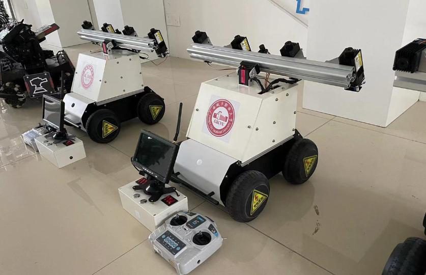 Closer view of two laser weeding robots on a tiled floor with a handheld transmitter and a video-monitor control box in front