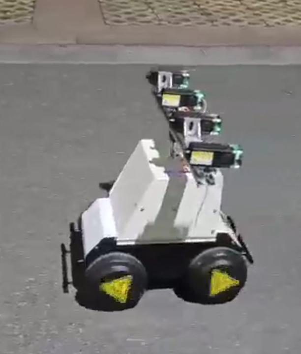 Blurry video frame from above of the white robot on asphalt, the laser beam pointing forward