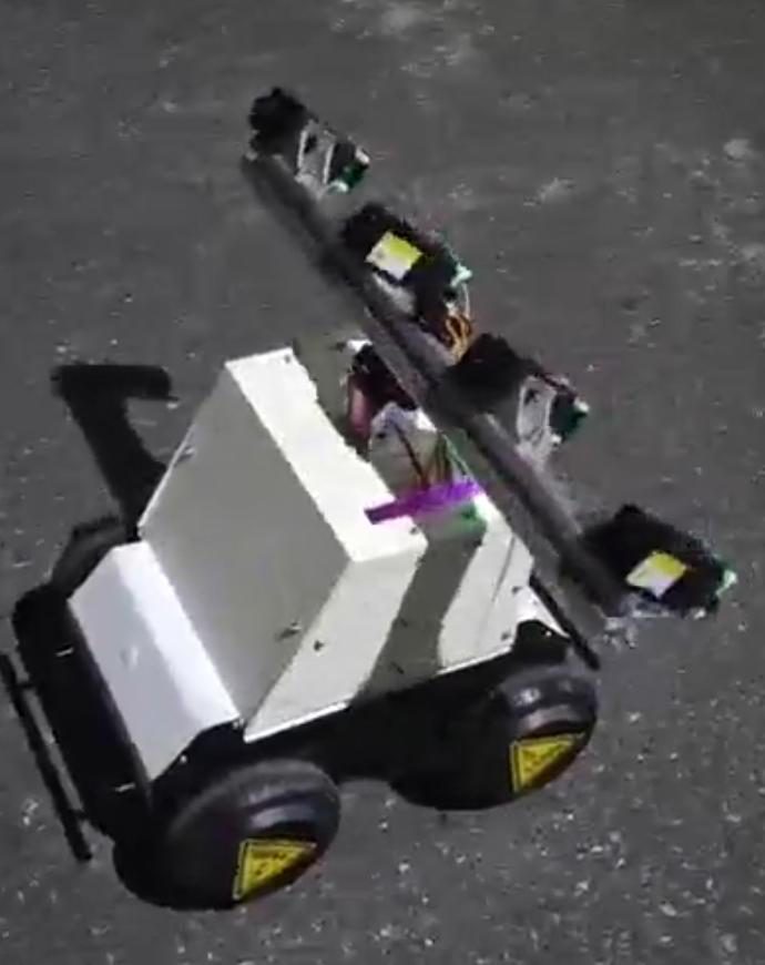 Video frame from above of the white robot on dark asphalt, laser beam angled across the body