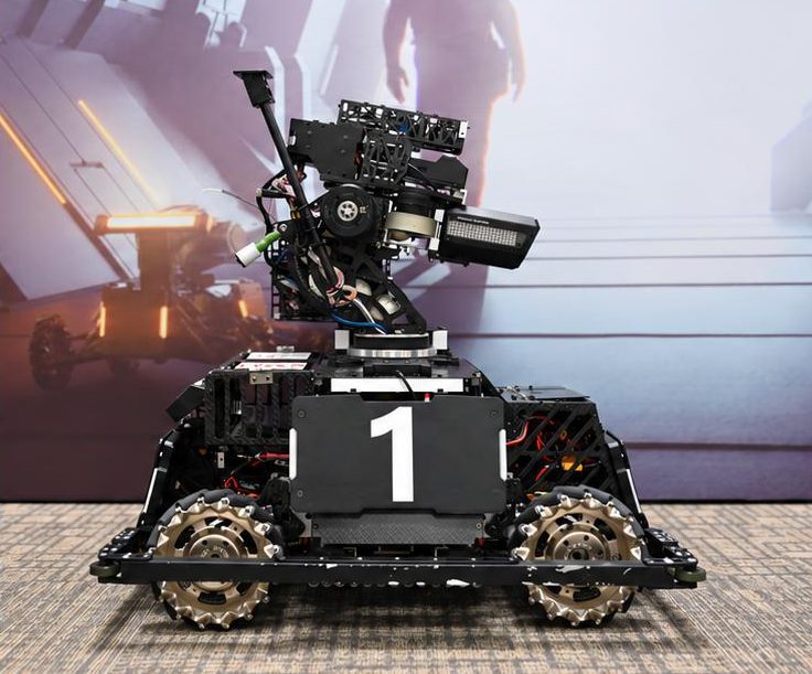 Side view of a black competition robot with a number '1' armor plate, gold mecanum wheels with angled rollers and a gimbal on top, standing on carpet in front of a printed backdrop