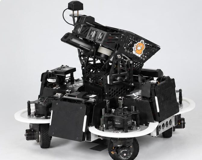 Black carbon-fiber competition robot with white bumper rings and a tilted gimbal on a grey studio backdrop; each wheel sits under its own steering motor