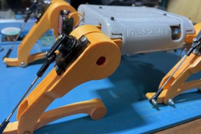 Low side view of the orange robot dog's legs and servo linkages on a blue workbench mat