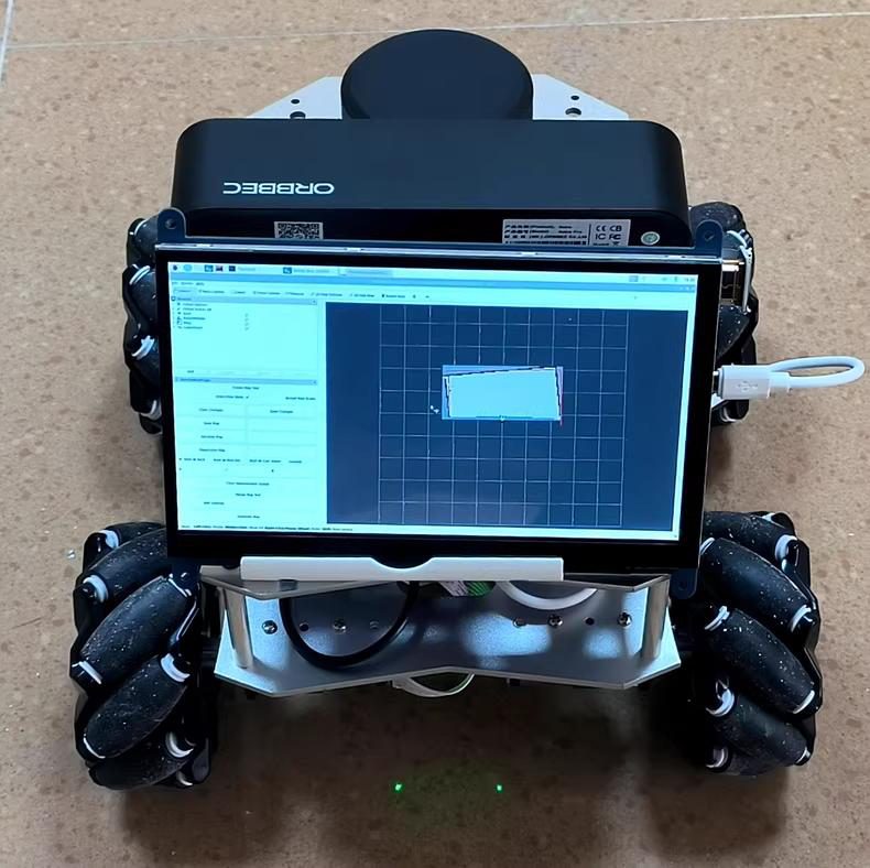 Front view of a mecanum-wheel robot on a tiled floor; a touchscreen on the front shows a mapping program with a grid, and a black depth camera sits on top