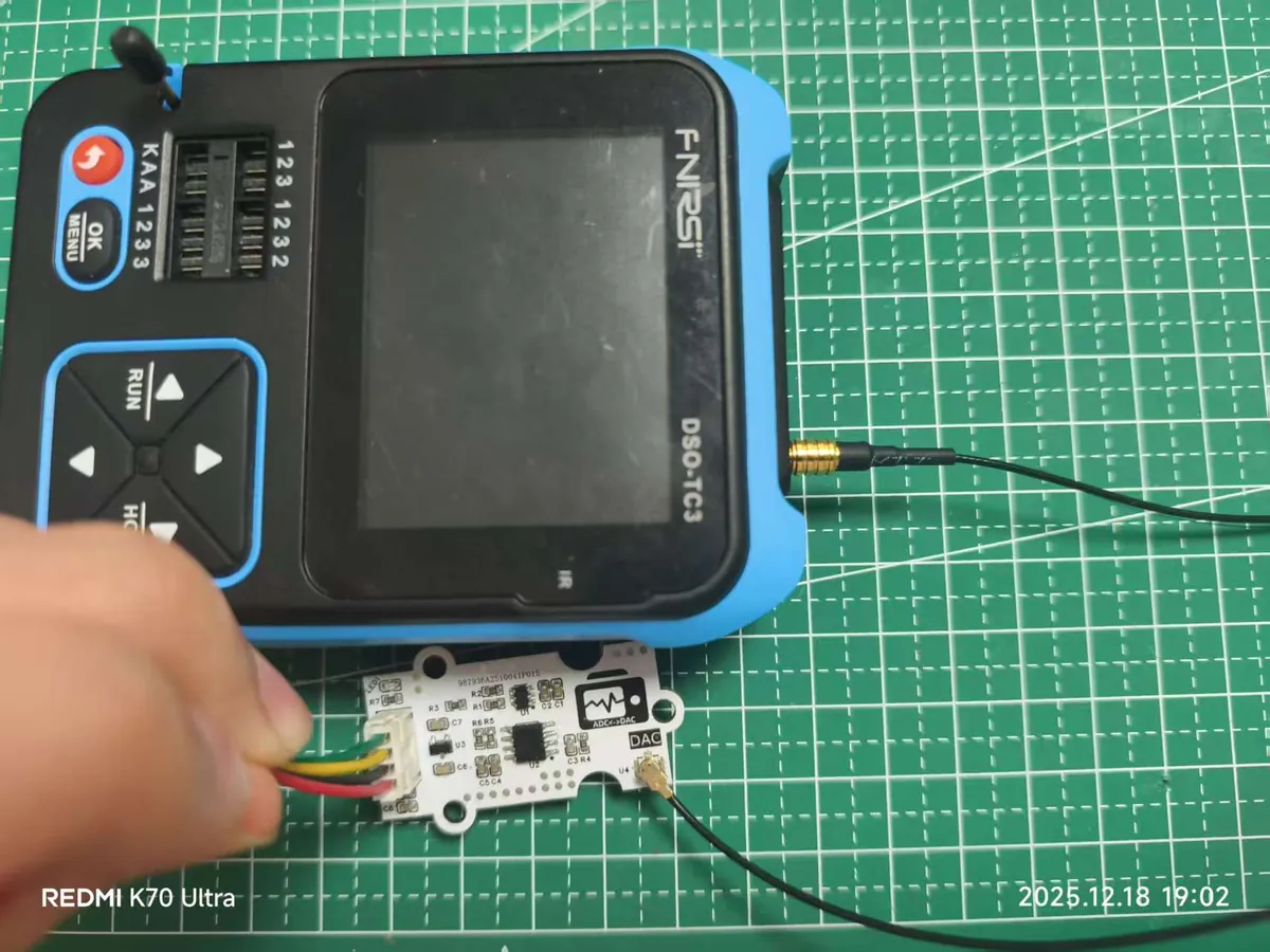 Handheld oscilloscope connected by a thin coaxial cable to a small DAC board, which is wired to a four-wire cable