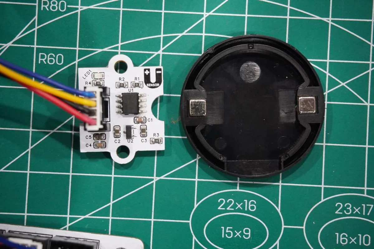 Sensor module on a cutting mat next to a round black cap holding two small block magnets