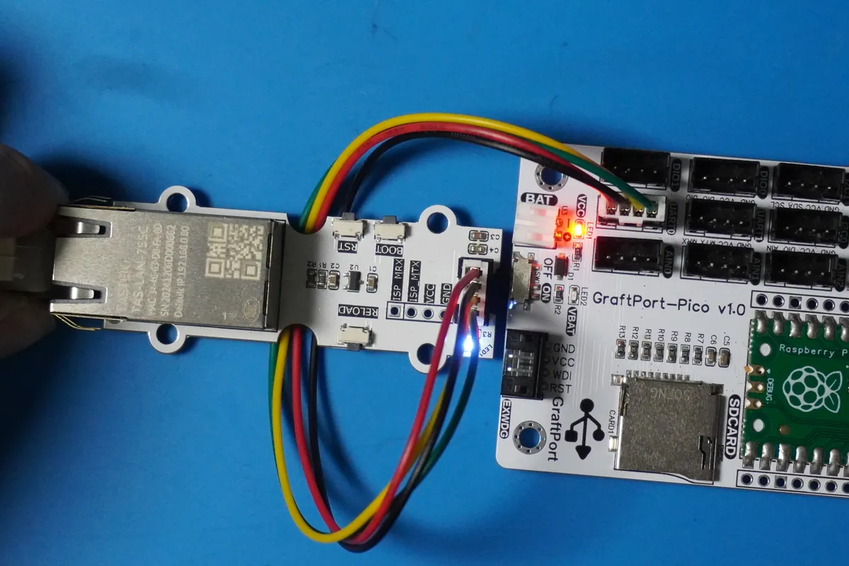 A TAS-LAN-755C Ethernet module with RJ45 jack on a small carrier, wired with a four-wire cable to the UART connector of a GraftPort-Pico board