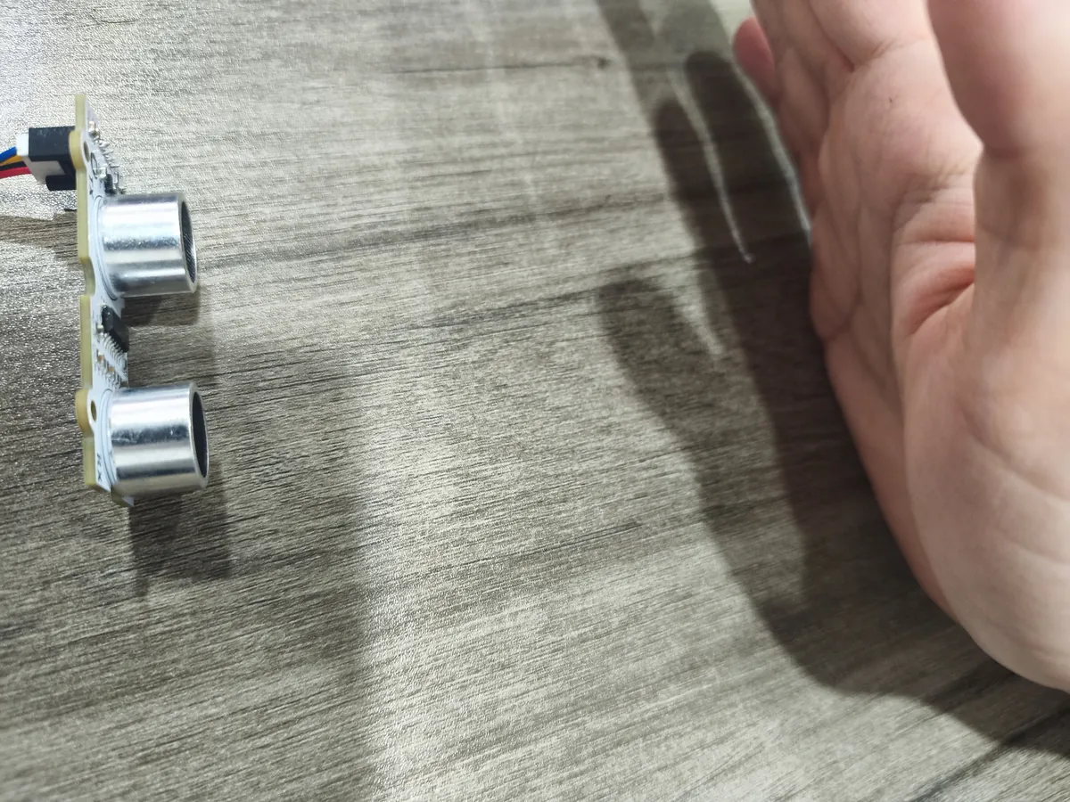 Ultrasonic module with two transducers standing on a table, with an open hand held a short distance in front of it